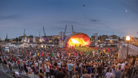 Main stage with bright orange lights, and thousands of people listening