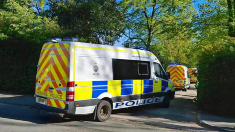 Three police vans in a row, parked in a a small side road. There are trees either side of the road.