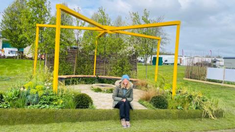 A smiling woman sits in front of a memorial garden