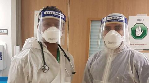 Dr Ajay Thomas and a colleague wearing white hospital scrubs and a face shield.