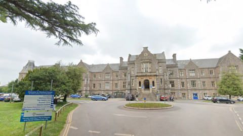 A large building behind a roundabout. There are cars parked around the car park. There is a sign which says "Welcome to Wonford House". 