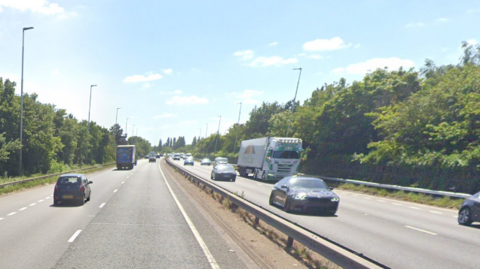 Parkway with cars on either side of a metal divider and trees bordering the end of the roads on each side and blue skies 