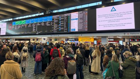 Passengers gaze up at departures board with arrival and departure information