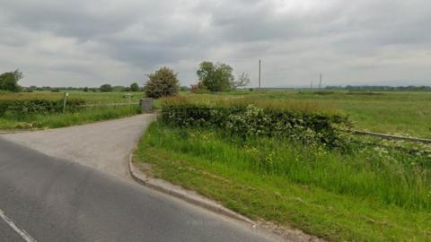 The entrance to the farm can be seen, with trees in the distance.