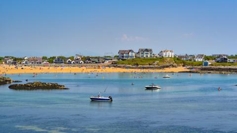 Bright blue sky over a broad sandy beach filled with people and boats out at sea