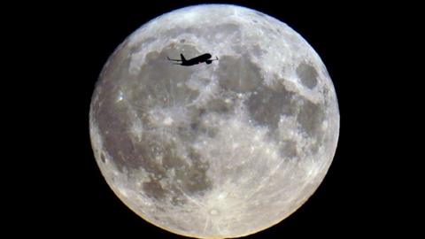 An aeroplane silhouetted across a bright full Moon in the night sky 