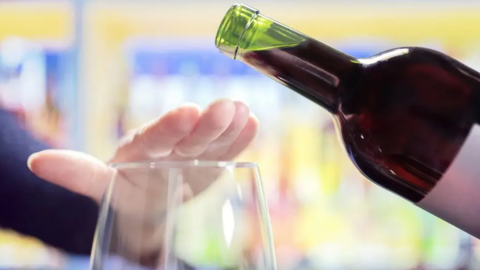 A person puts their hand over the top of a wine glass as wine is to be poured from a bottle.