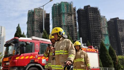 Firefighters walk near the site of a major fire at Wang Fuk Court housing complex,