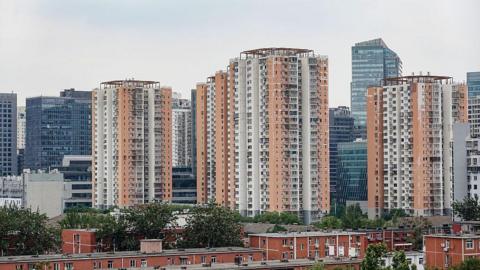 Several orange and white high-rise apartment buildings stand in front of modern high-rise buildings in Beijing