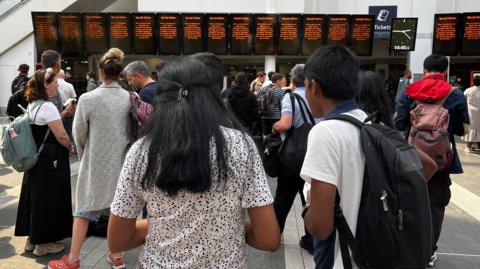 A crowd stands in front of a row of screens that should show train departure times but all say "Special Notice" on them.