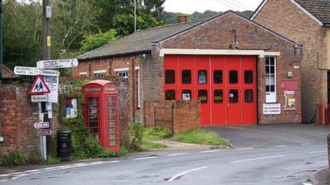 Cranborne fire station is a small brick building on a bend in a village road, with an adjacent red phone box and a signpost giving directions to Dorset towns and villages.