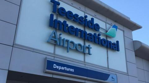 The entrance to Teesside International Airport. The sign with the airport's name stands above the entrance. Another sign reads, departures.