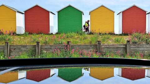 People walk past multi coloured beach huts in Eastbourne on 3 June