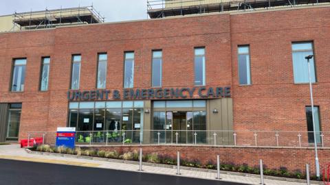 New-build red-brick building with a sign reading "Urgent and Emergency Care" above the entrance.