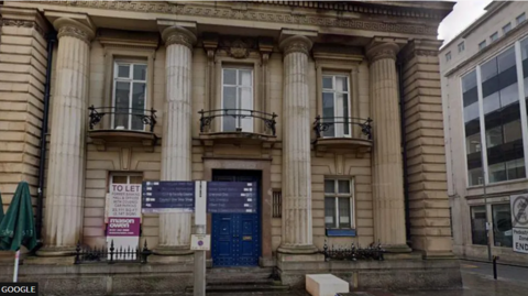 A general view of the former Bank of England building on Liverpool's Castle Street. It is an ornate building with classical columns either side of a large blue doorway.