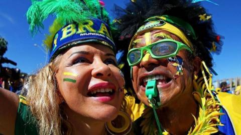 A close-up shot of two Brazil fans wearing green and yellow clothes, as well as feather headdresses.
