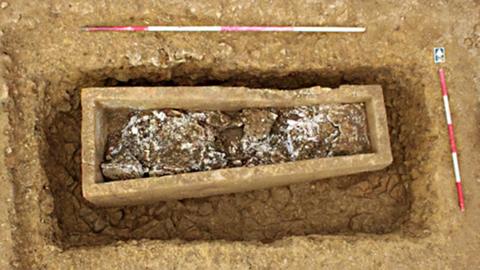 A dug-up grave with a stone coffin inside it and red and white markers placed around the grave.