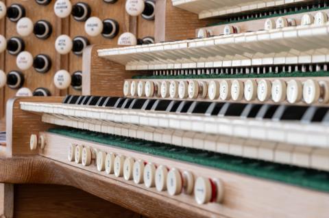Multiple layers of black and white organ keys. There are rows of numbered buttons under each row of keys and a grid of white handles to the side of the keyboards.
