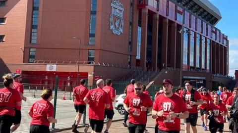 Scores of runners in red shirts emblazoned with the number "97" run past Anfield Stadium.