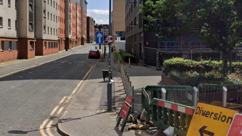 A residential street with student accommodation blocks on one side. There are a number of traffic signs including one indicating a diversion. 