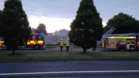 red and yellow fire trucks and firefighters looking onto a smokey site