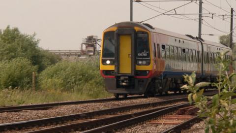 A two-carriage East Midlands Railways train with yellow frontage travels along a railway line towards the camera.