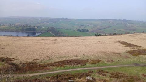 A large empty moorland with dry brown grass across most of it. A reservoir is visible in the distance.