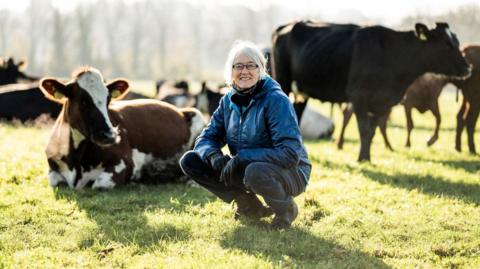 Mary Quicke of Quicke's Cheeses crouching in front of cows in a field