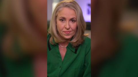 Sarah Smith has shoulder-length blonde hair and is wearing a green jacket. She looks directly at the camera.