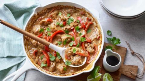 Peanut butter chicken in a white pan with a wooden spoon 