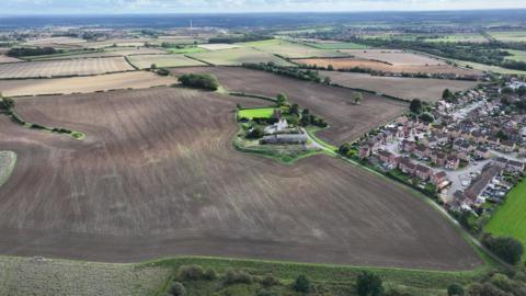 An aerial image of land that is set to be developed near Clowne. It is mostly brown fields, with homes to the right.