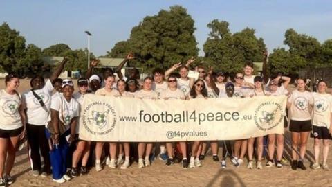 A group of people standing together, holding a large white banner with the words "football for peace".