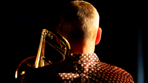 The back of an artist performing with a brass instrument