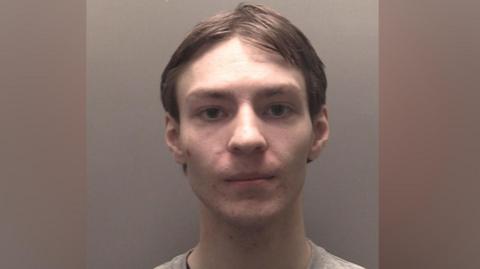 A police custody photograph of Darren Rigby who has brown hair and is wearing a grey jumper over a black t-shirt