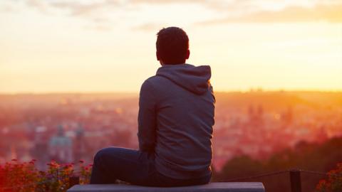 A young man sits overlooking a city at sunrise