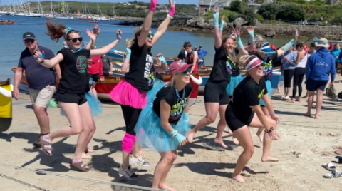 A number of people jumping in the air in fancy dress including tutus on a beach.