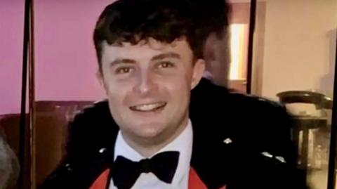 Captain Philip Gilbert Muldowney smiles as he looks into the camera, with short dark hair, wearing a dress suit and bow tie. 