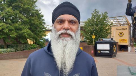 Manny Singh Kang wearing a blue top, with a long beard, standing near Molineux
