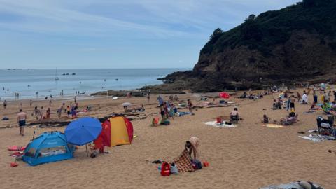 Dozens of people at the beach with the sea on the left and cliffs on the right.