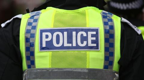 Back of police officer wearing a hi-vis yellow and blue jacket with "Police" emblazoned on the back