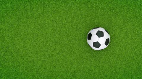 A black and white football on a bright green artificial pitch.