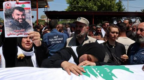 A woman grieves over a coffin draped with a Lebanese flag, while another holds up a picture of the deceased individual killed in an Israeli air strike, at a funeral in Tyre, Lebanon (30/04/26)