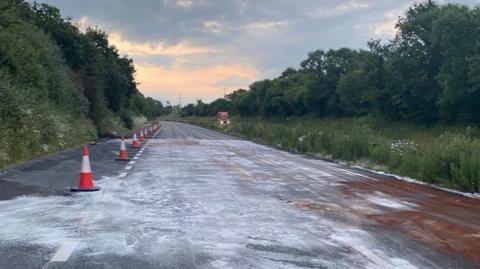 A road covered in brown and white residue, with traffic cones on the side.