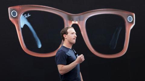Meta CEO Mark Zuckerberg on a stage describing Meta's Ray-Bans, a large image of which is being shown behind him.
