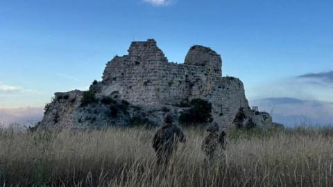 Israeli military handout showing two Israeli soldiers standing in long grass. Ahead of them is a ruined fortress.