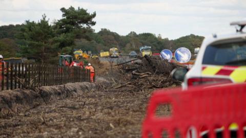 Men in high vis in a burnt forest working on the road.