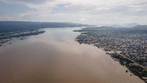 An aerial view of a wide River Niger flowing past a city on the right bank.