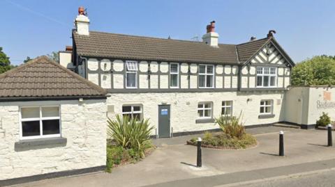 A two-storey white painted brick building with grey wood features and a pitched roof on one end.