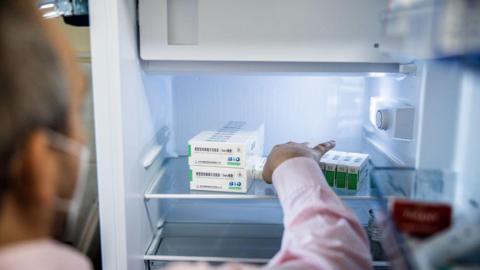 A medical worker removes a box of vaccines from a refrigerator.
