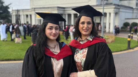A mother and daughter in ceremonial robes in front of De Montfort Hall in Leicester